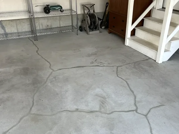 Wide view of cracked basement floor near stairs showing extensive crack pattern